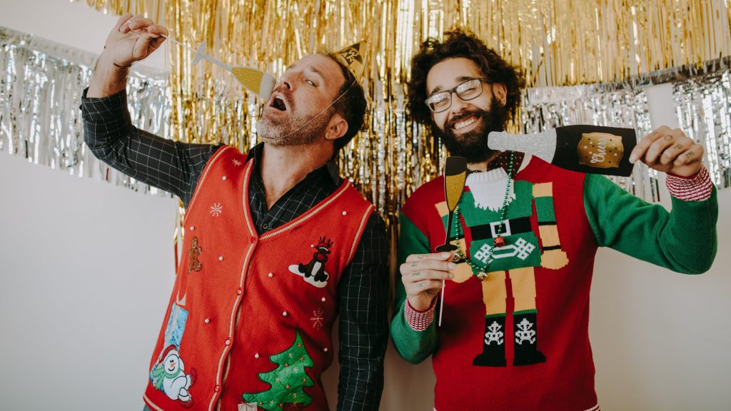 Two men wearing ugly Christmas sweaters holding photo booth props